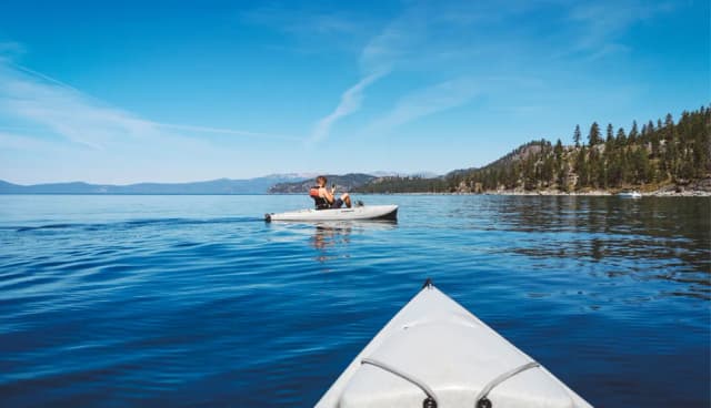 Kayakers paddling on calm blue waters surrounded by forested mountains in Tahoe Vista, CA.