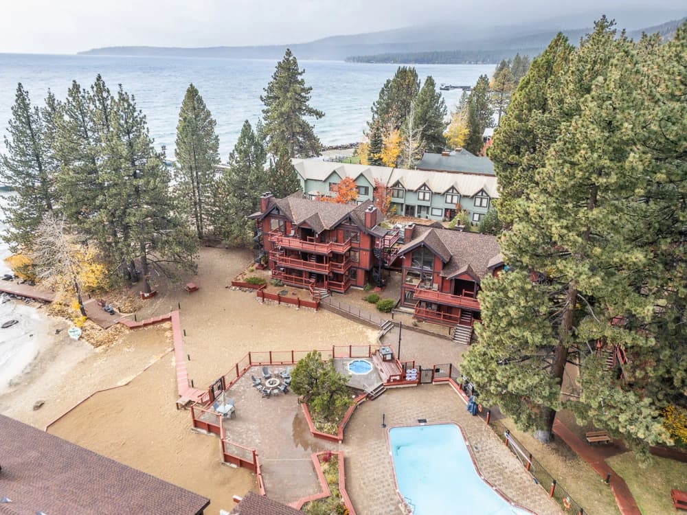 Aerial of red lakeside lodges with courtyard, hot tub, and pool by the beach