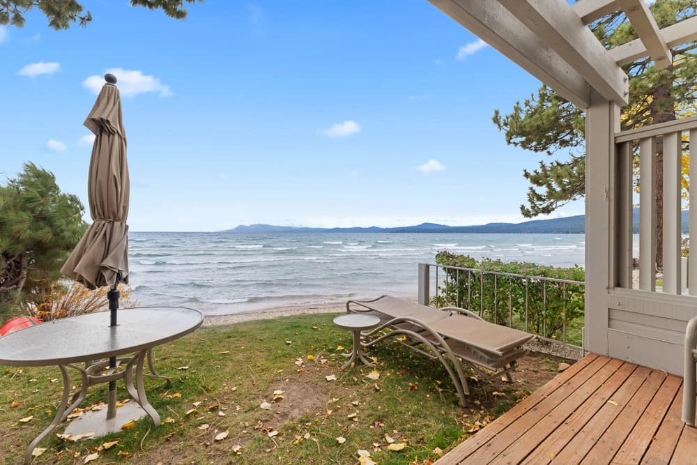 Lakeside patio with loungers and umbrella table on grass beside the sandy beach