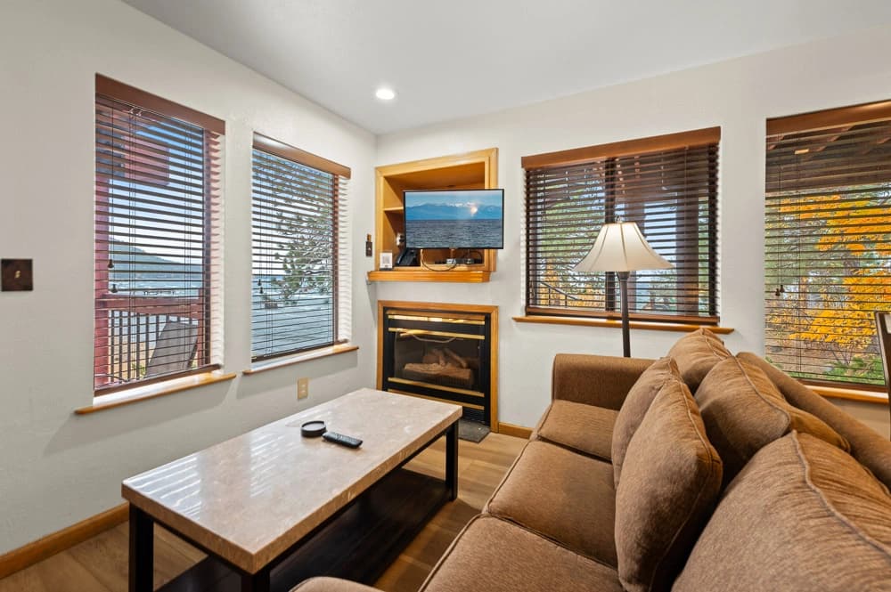 Cozy living room with gas fireplace, sofa, and lake views through corner windows at Tahoe Edgelake Beach Club
