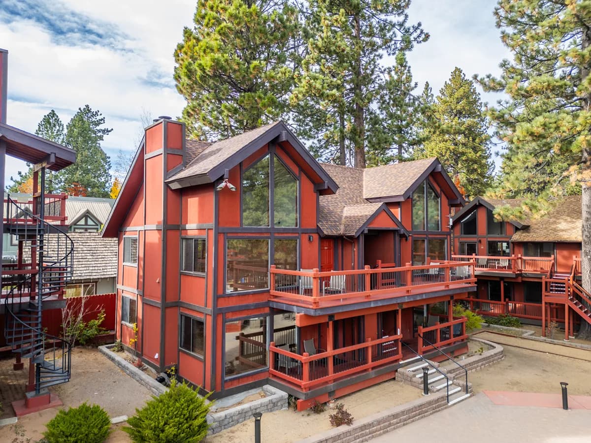 Outdoor fenced pool framed by pine branches, with lodge buildings and Lake Tahoe beyond