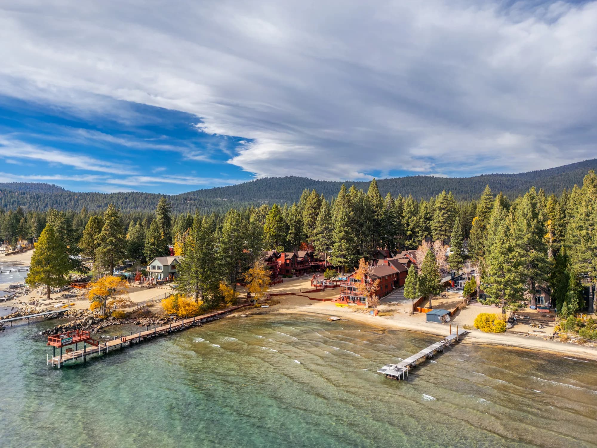 Lakeside cabins surrounded by pine trees with a wooden dock extending into the water.